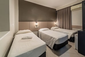 Habitación de hotel con dos camas individuales, un amplio ventanal con cortinas, un escritorio empotrado y un aire acondicionado de pared.