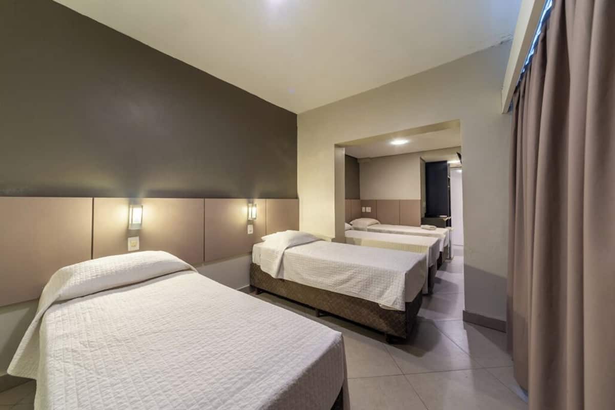 Habitación de hotel con tres camas, un espejo grande y vista al pasillo.