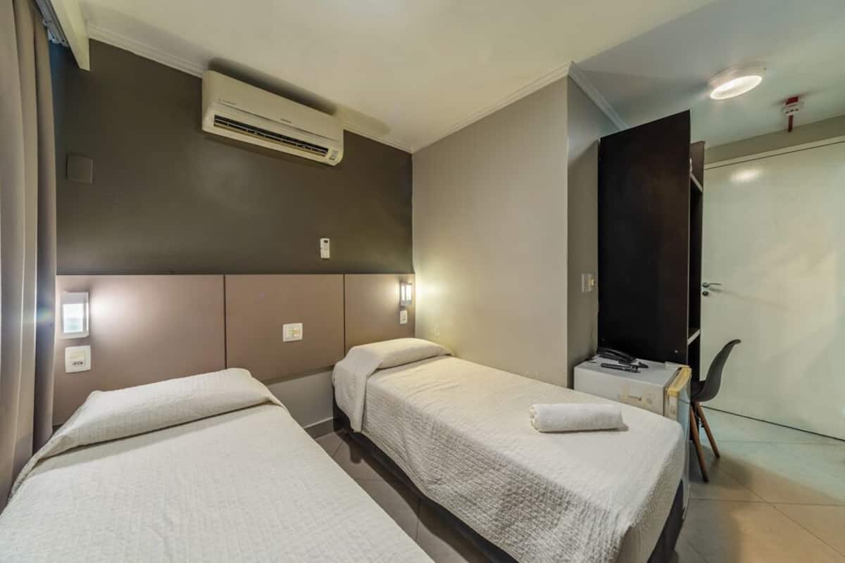 Una habitación de hotel con dos camas, aire acondicionado, un escritorio con silla y un armario.