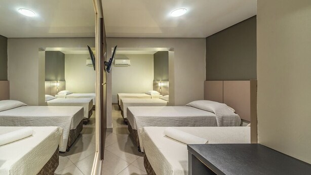 A mirrored room with four beds, a dark wooden desk, and a white tiled floor. - Hotel Minuano Express (Porto Alegre)