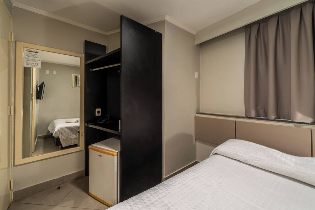 Un dormitorio con cama, armario, espejo y ventana con cortinas.
