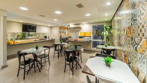 A modern kitchen with a dining area, featuring a central island, chairs, and a TV mounted on the wall. - Hotel Minuano Express (Porto Alegre)