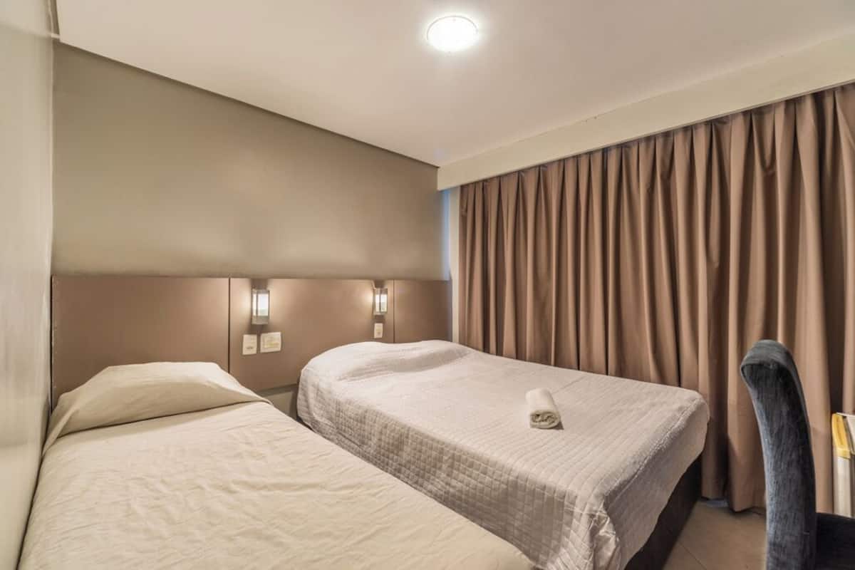 Una habitación de hotel con dos camas, cabecero, lámpara de pared y cortina.