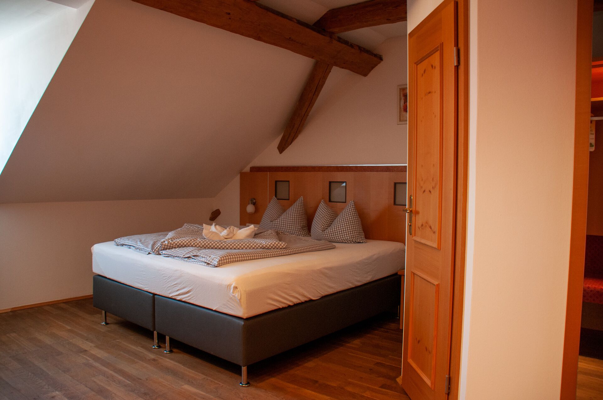 A bedroom with a sloped ceiling, a bed with checkered bedding, and wooden beams.