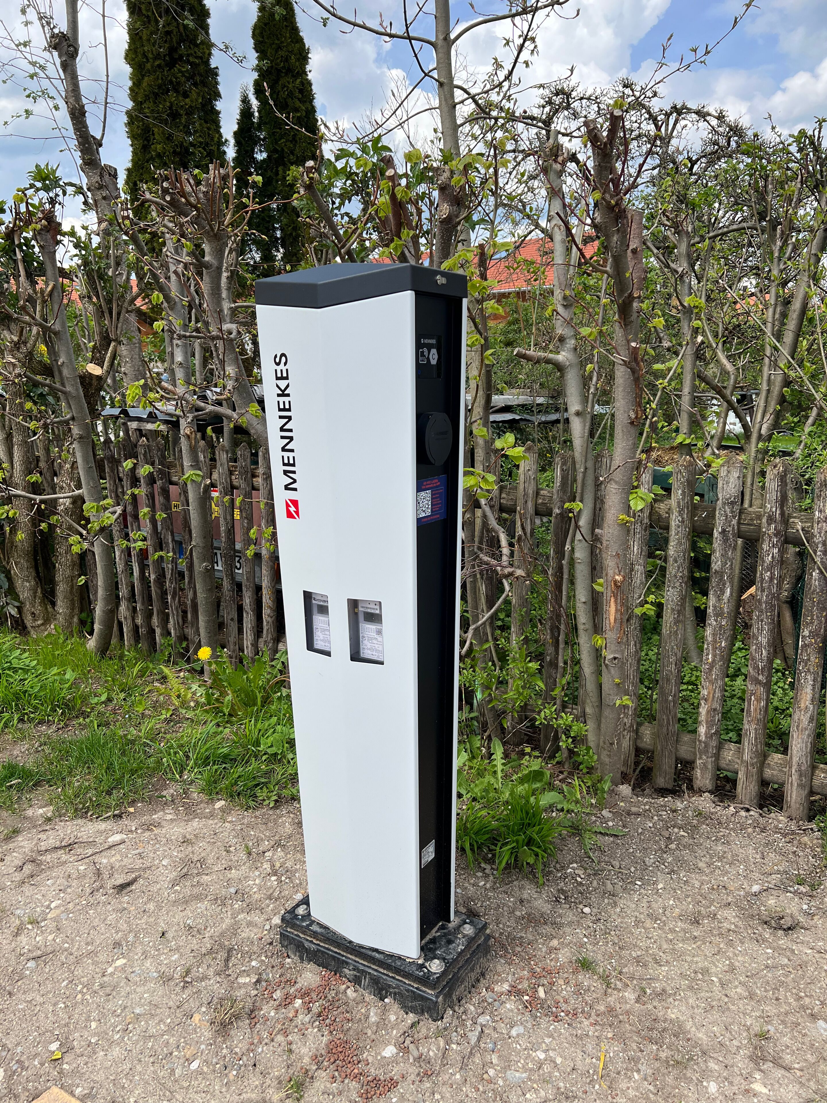 A white electrical box with the brand 'MENNEKES' and two control panels, surrounded by trees and a fence.