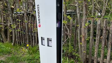 A white electrical box with the brand 'MENNEKES' and two control panels, surrounded by trees and a fence.