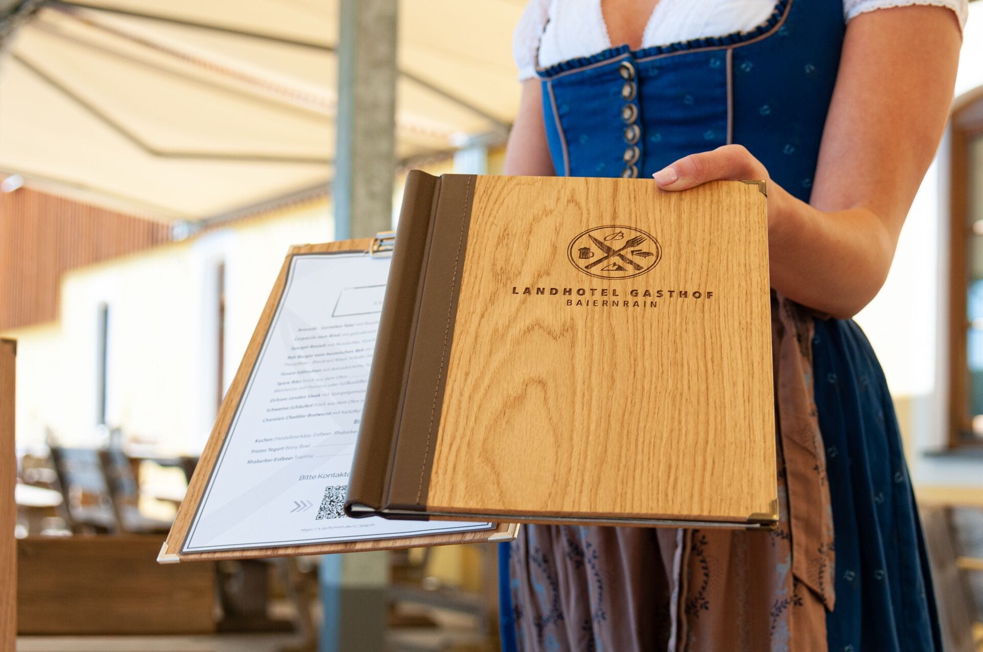 Eine Person hält eine Holzmappe mit dem Text "LANDHOTEL GASTHOF BAIERNRAIM".