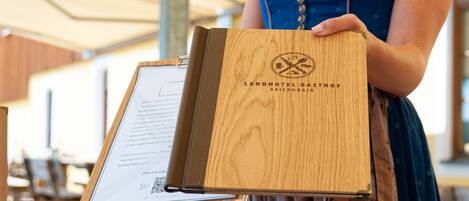 Una persona sosteniendo una carpeta de madera con el texto "LANDHOTEL GASTHOF BAIERNRAIM".