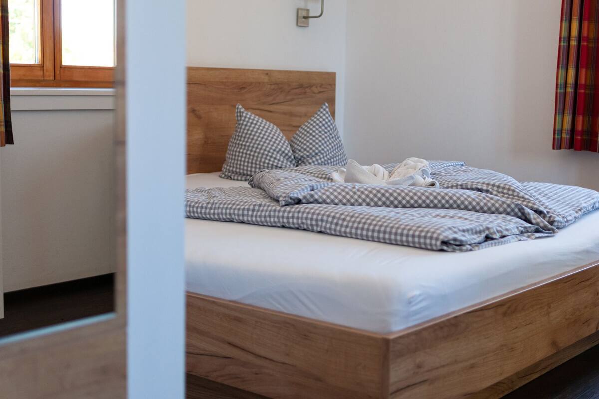 Un lit bien fait, avec une literie à carreaux et des oreillers, une tête de lit en bois et une fenêtre avec des rideaux.