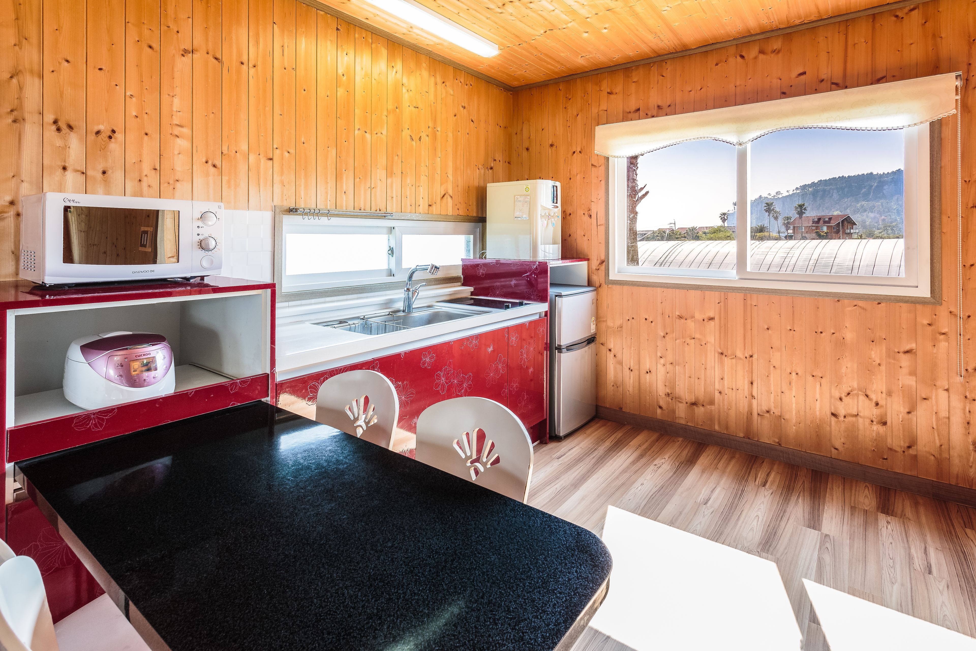 Una cocina compacta con paredes de madera, un comedor con mesa negra y una ventana con vistas a colinas.