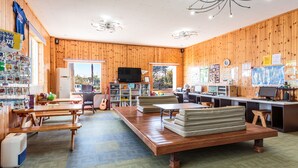 A cozy, well-lit room with wooden walls, a large wooden table, multiple seating options, and a television. - Olleh Windmill Pension & Guesthouse - Hostel (Seogwipo)