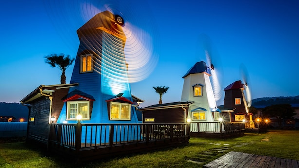 A series of uniquely designed houses with prominent windmill-like structures, each featuring a distinct architectural style and illuminated windows. - Olleh Windmill Pension & Guesthouse - Hostel (Seogwipo)