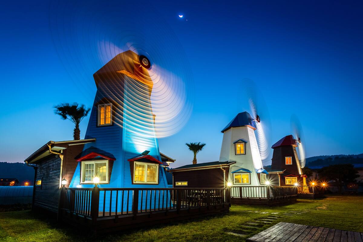 Une série de maisons à l’architecture originale, chacune dotée d’une structure distinctive rappelant un moulin à vent et de fenêtres illuminées, et présentant un style architectural unique.