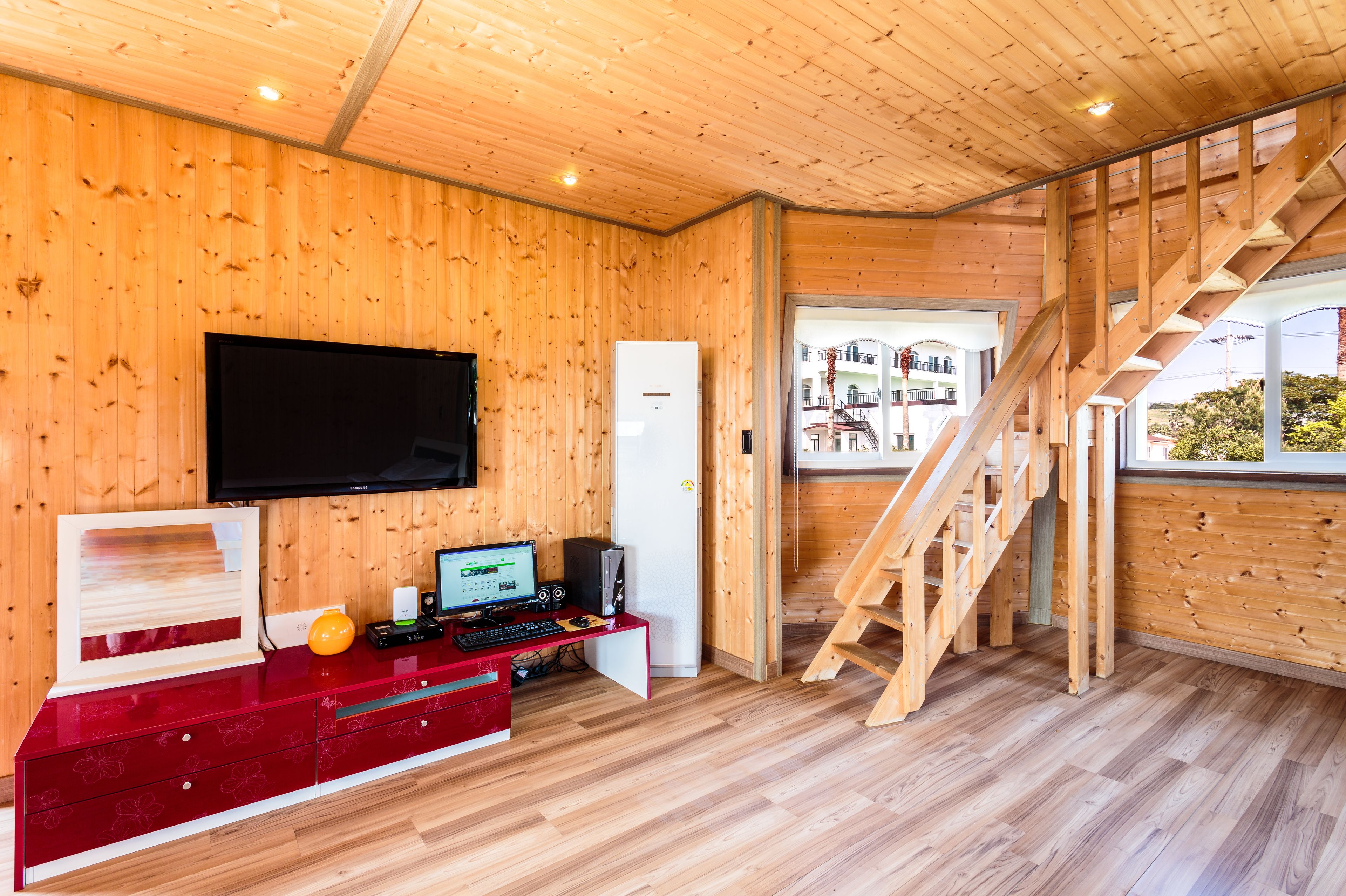 A modern room with wooden walls, a flat-screen TV, a desk with a computer, and a wooden staircase.