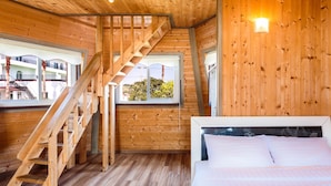 A wooden interior with a bed, a staircase, and windows offering a view of buildings outside. - Olleh Windmill Pension & Guesthouse - Hostel (Seogwipo)