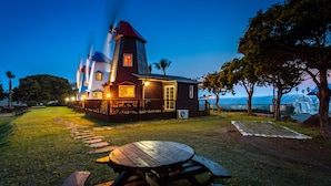 A wooden house with a tower, a covered area, and a picnic table in the foreground. - Olleh Windmill Pension & Guesthouse - Hostel (Seogwipo)