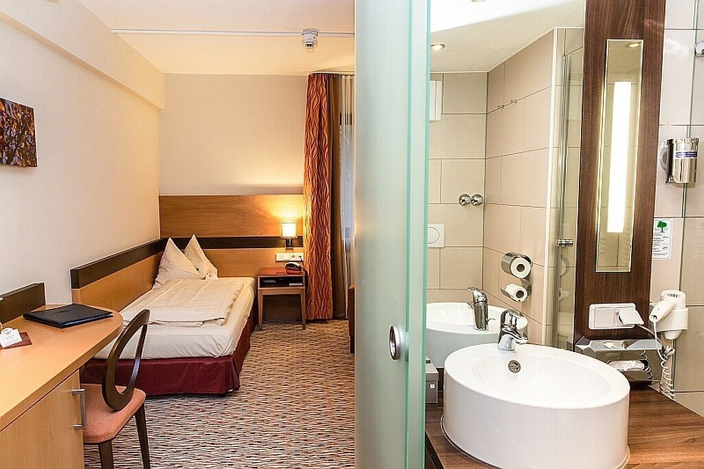 Une chambre d’hôtel comprenant un lit, un bureau, une chaise et une salle de bain avec un lavabo et un miroir.