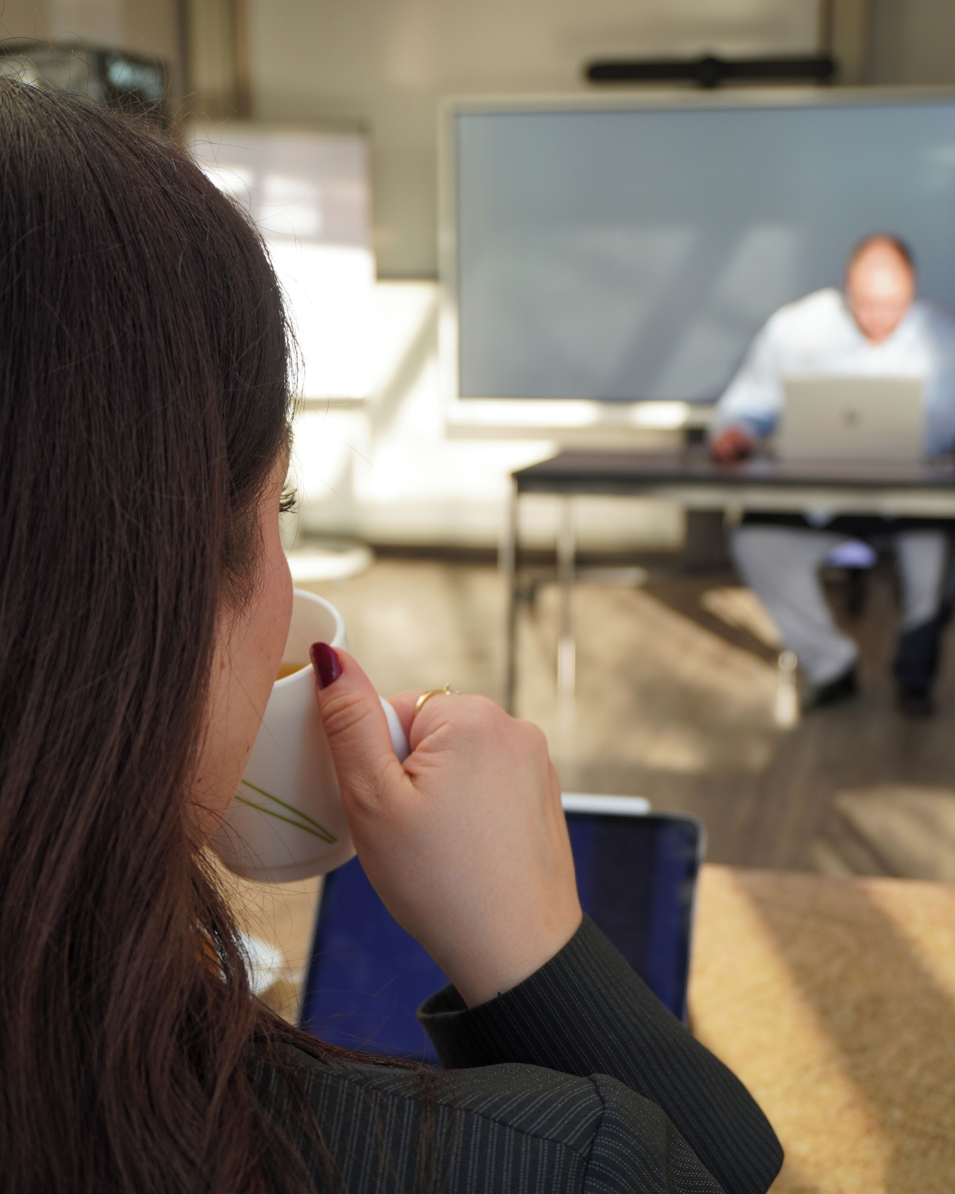 Eine Person sitzt an einem Schreibtisch mit einem Laptop, einem Whiteboard und einem blauen Stuhl im Hintergrund.