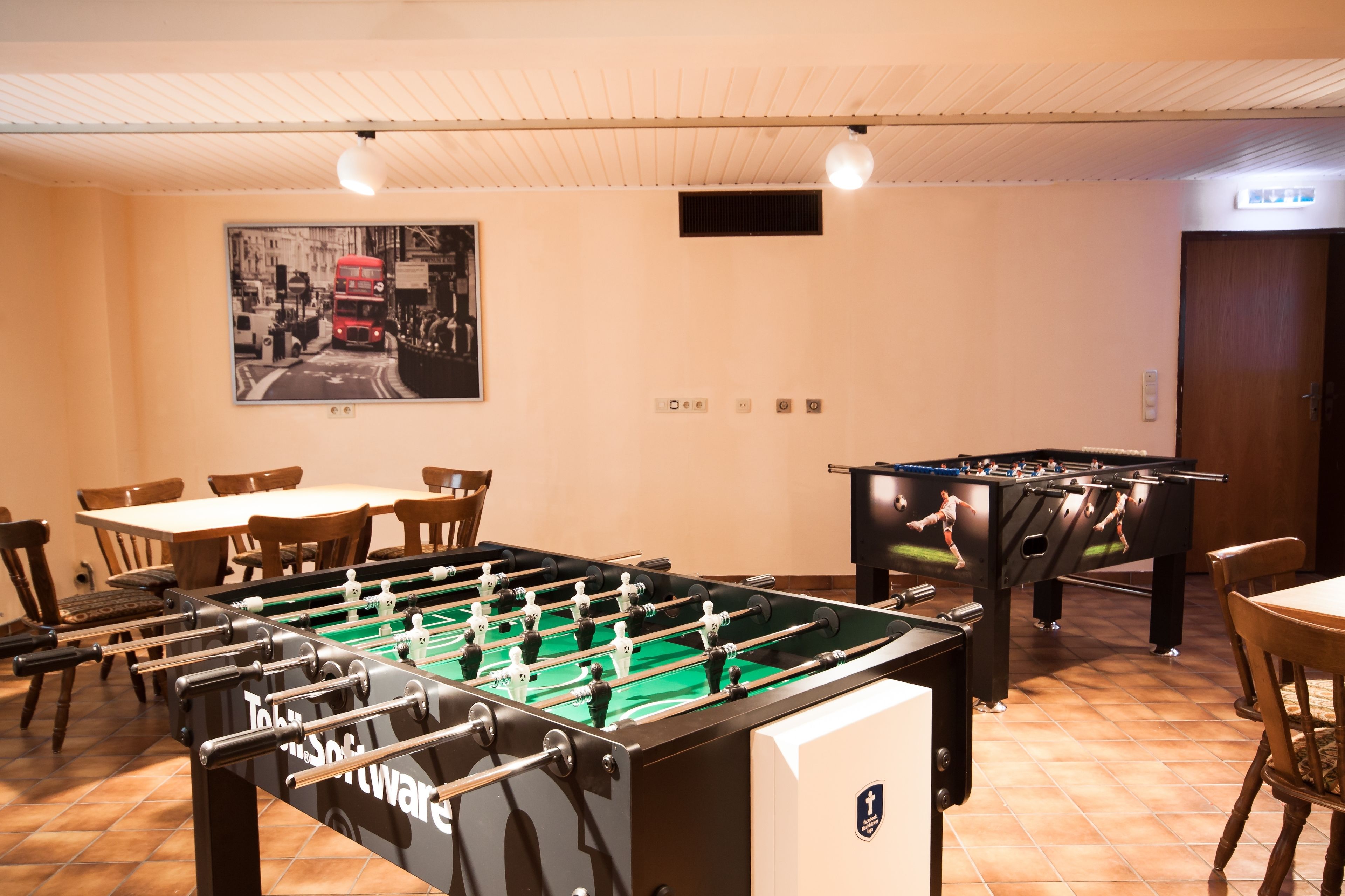 A room with a foosball table, a pool table, and a dining area with chairs and a table.