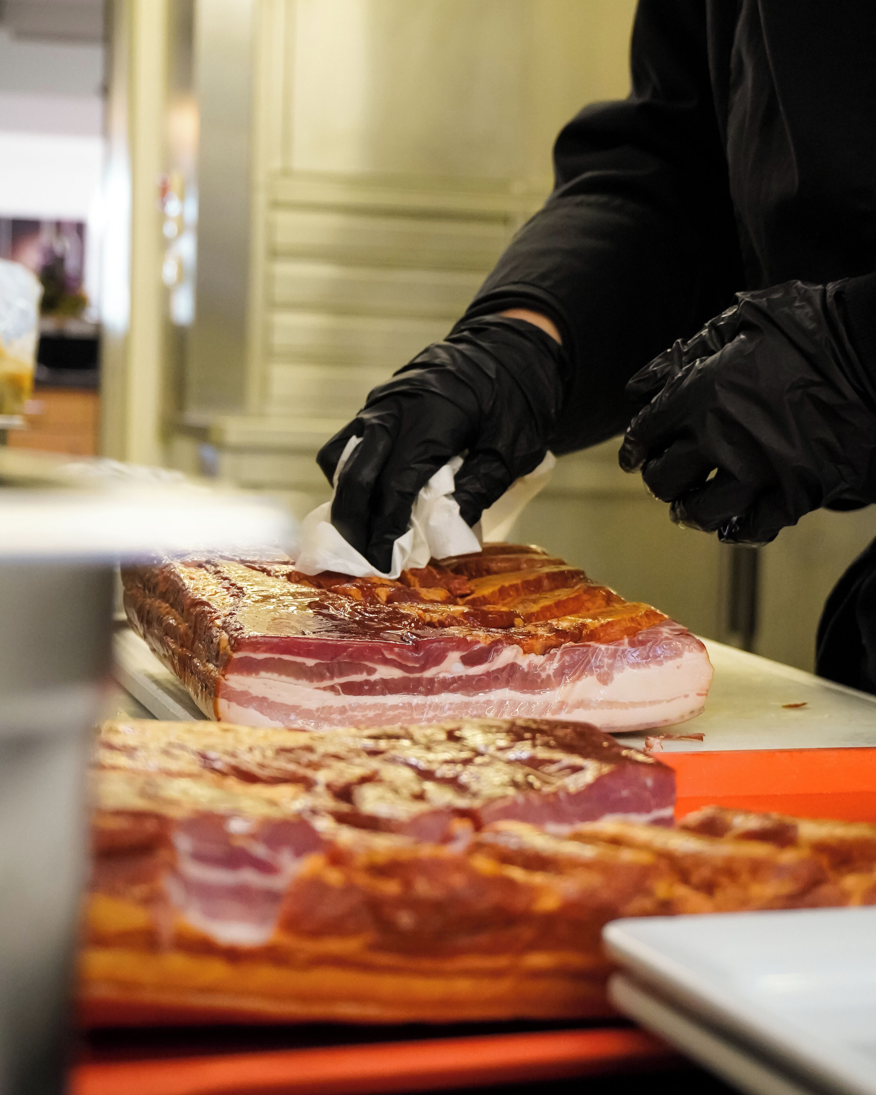 A person handling a large piece of meat, likely pork, with gloved hands.