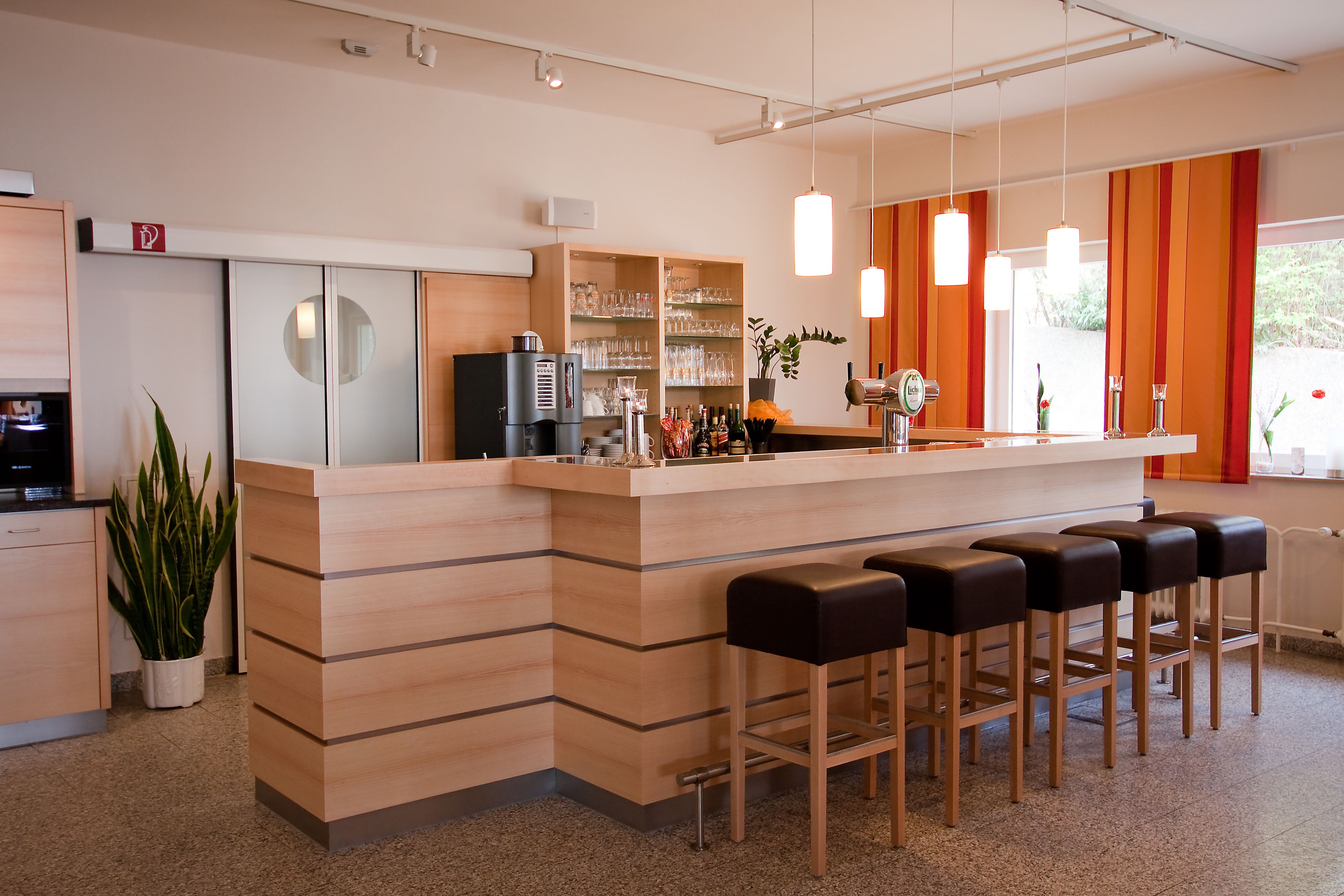 A modern bar area with a wooden counter, bar stools, and shelves with glasses and bottles.