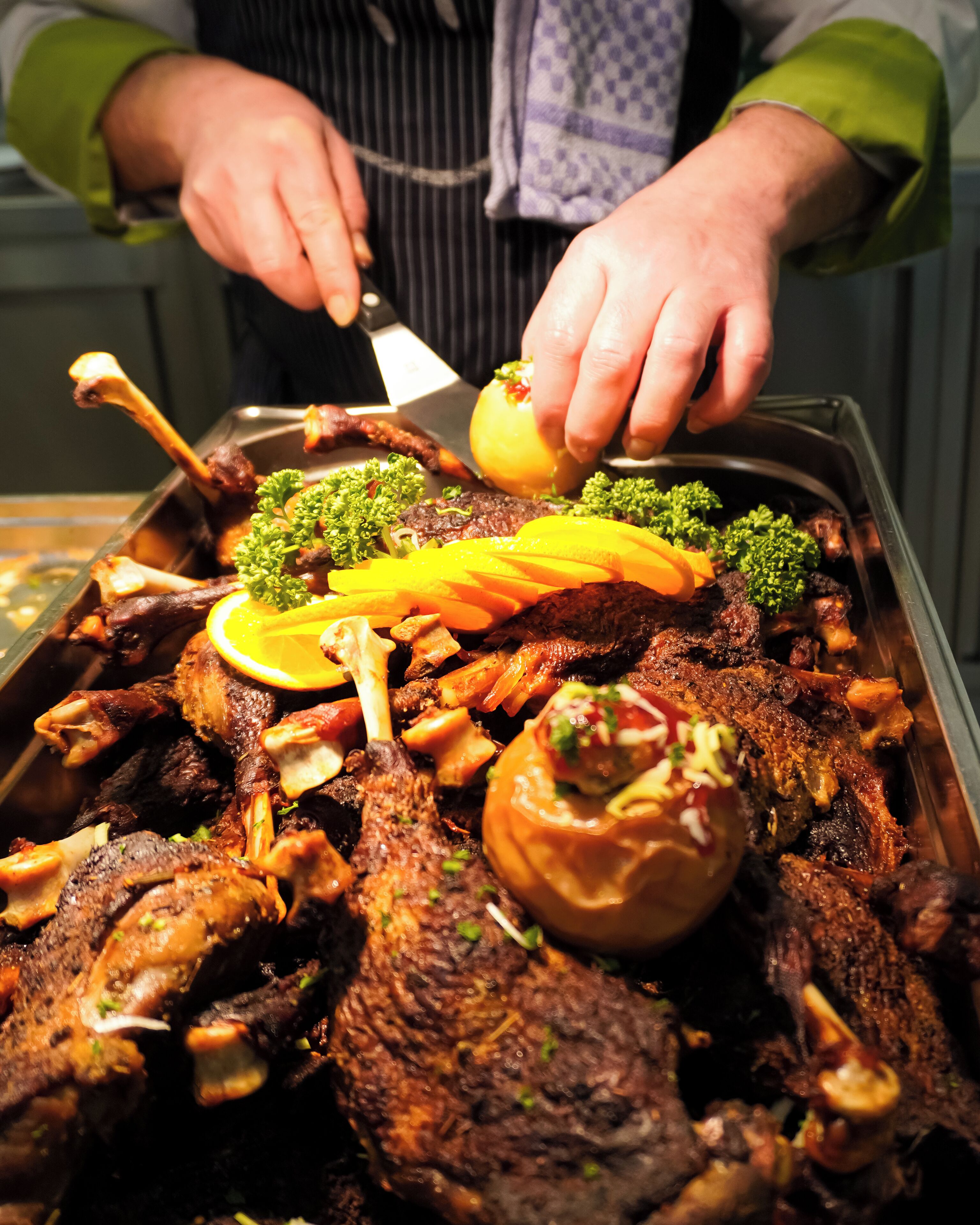 A person serving a large platter of roasted meats and vegetables.