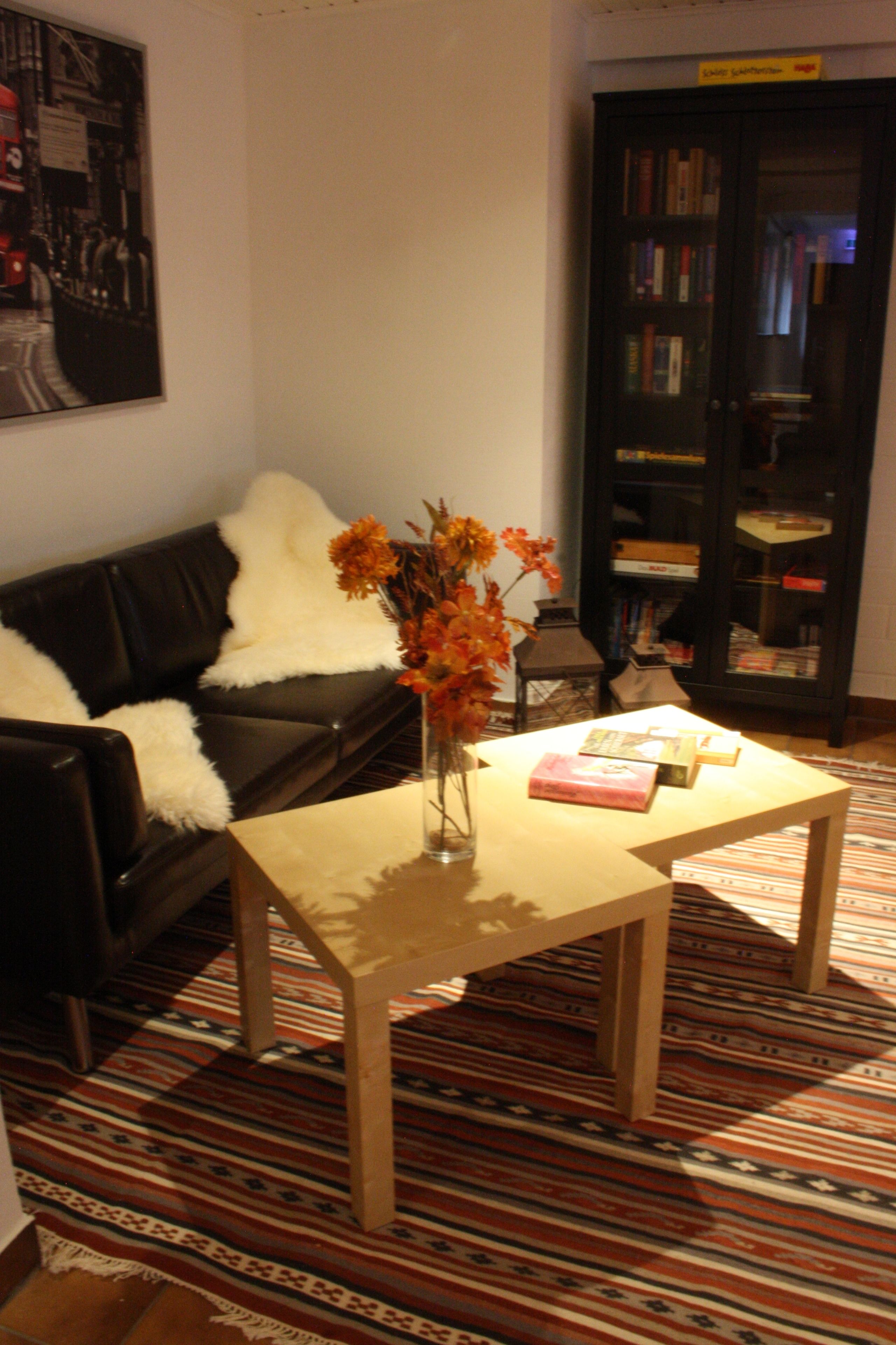 Una sala de estar con un sofá de cuero negro, una mesa de centro de madera, un jarrón con flores y una estantería.