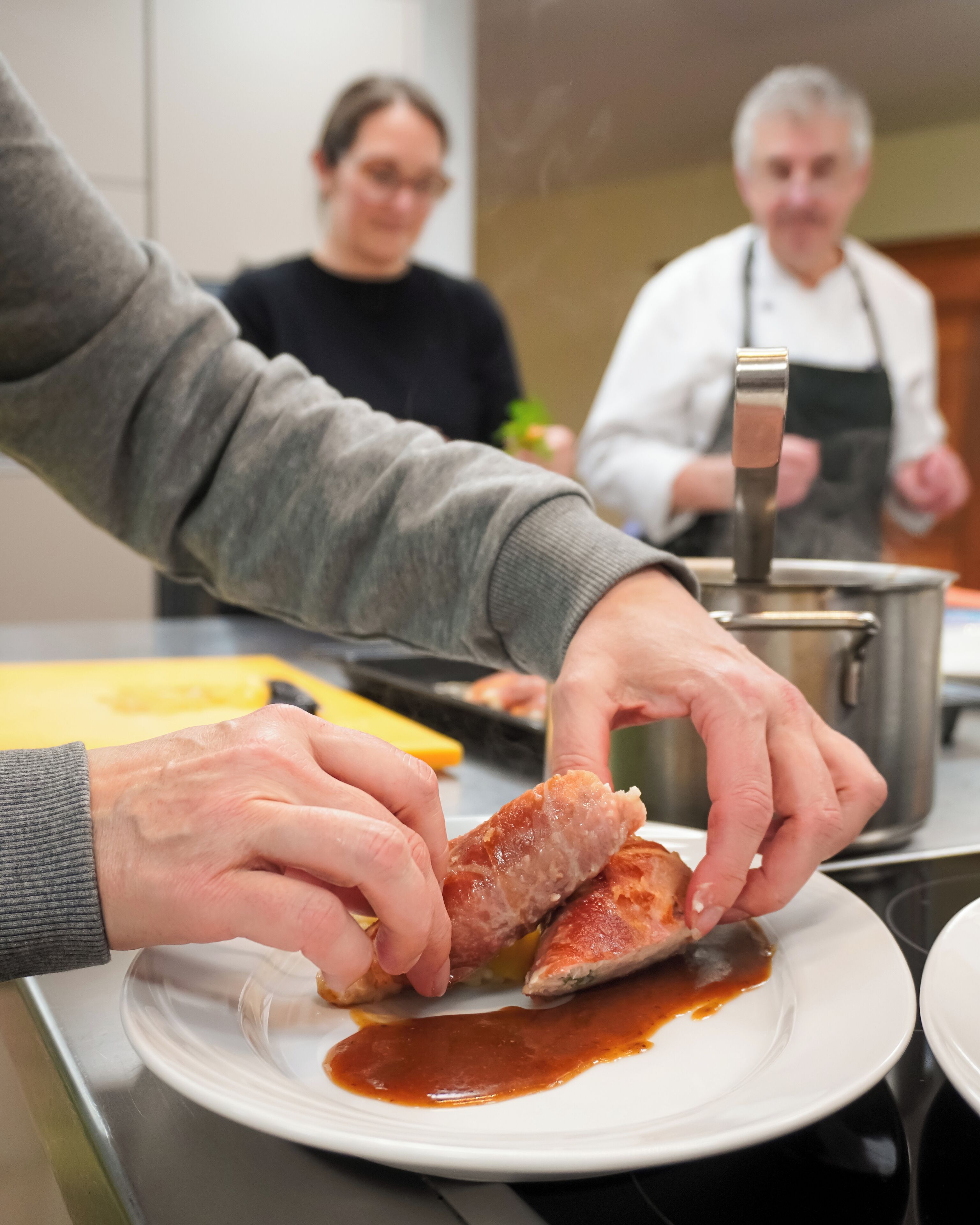 A person preparing food, specifically handling a piece of meat on a plate with sauce.