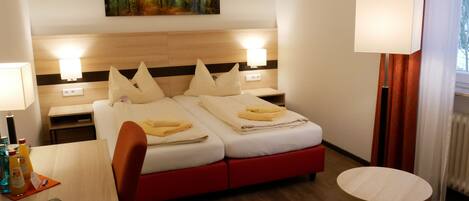 Een hotelkamer met twee bedden, een bureau, een stoel, een nachtkastje, een lamp en een schilderij aan de muur.