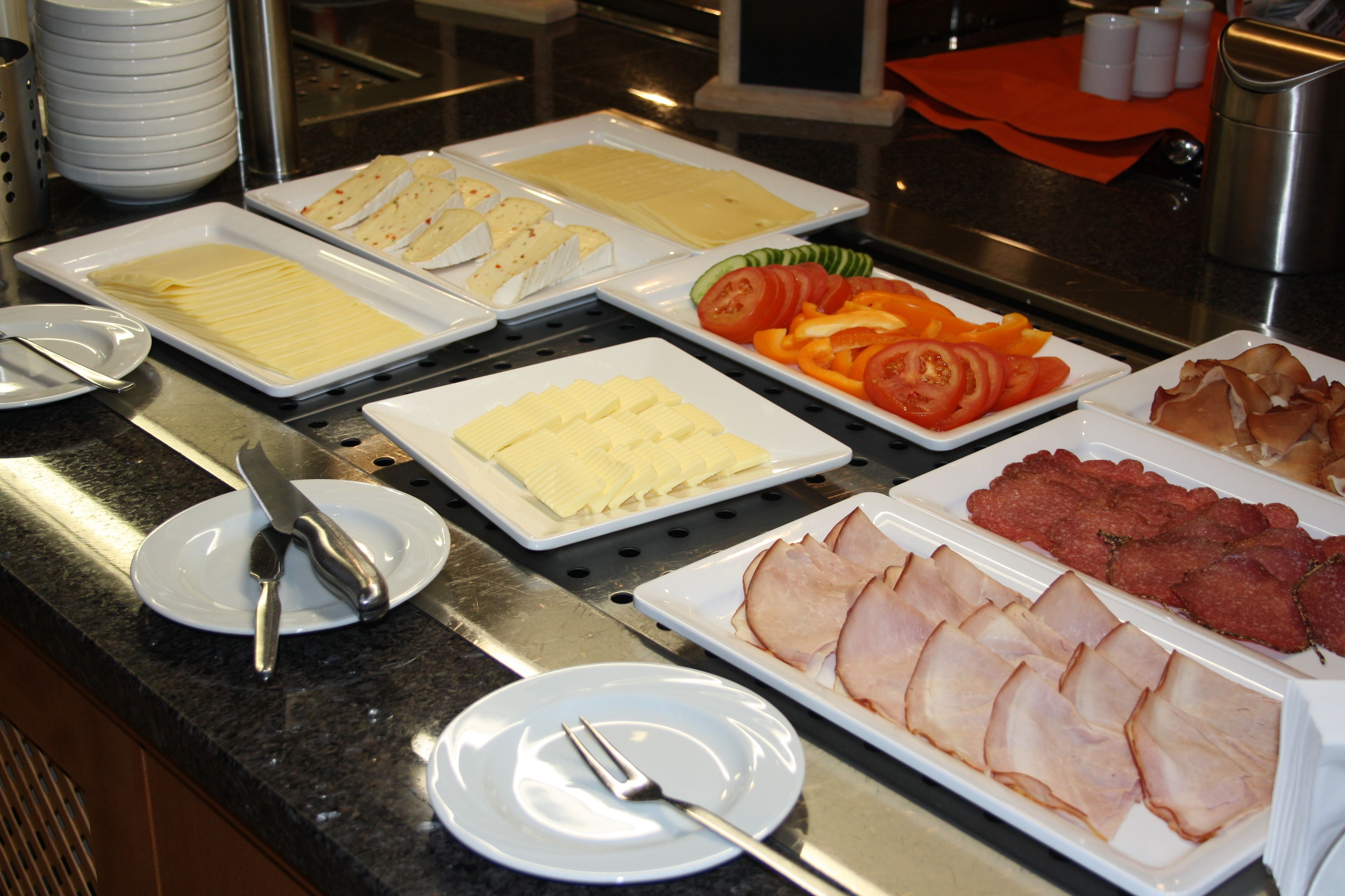Un bufé con distintos alimentos, como queso, jamón y verduras.