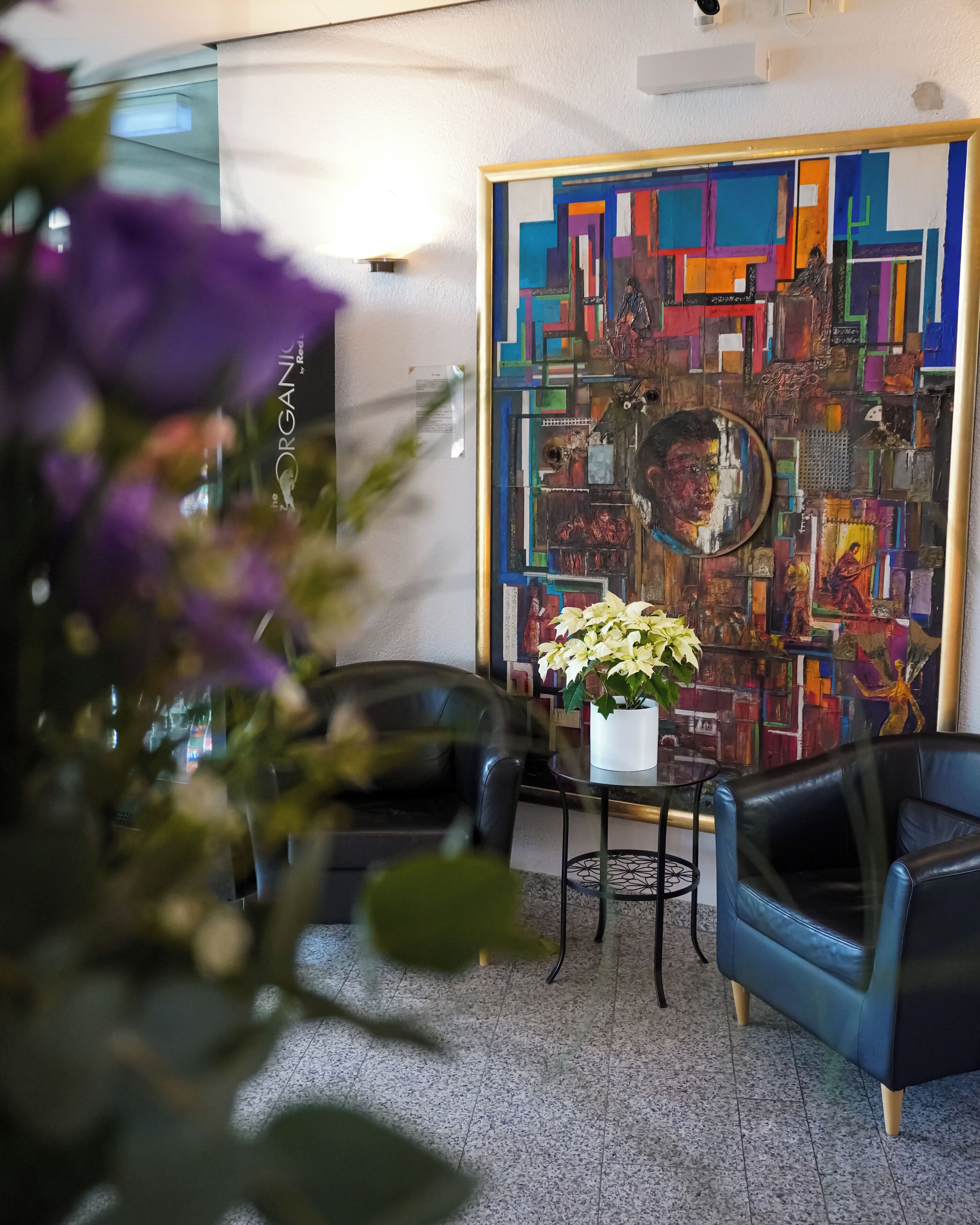 Un salon moderne avec un grand tableau abstrait, deux fauteuils en cuir, une petite table sur laquelle est posé un vase de fleurs et une plante en pot.