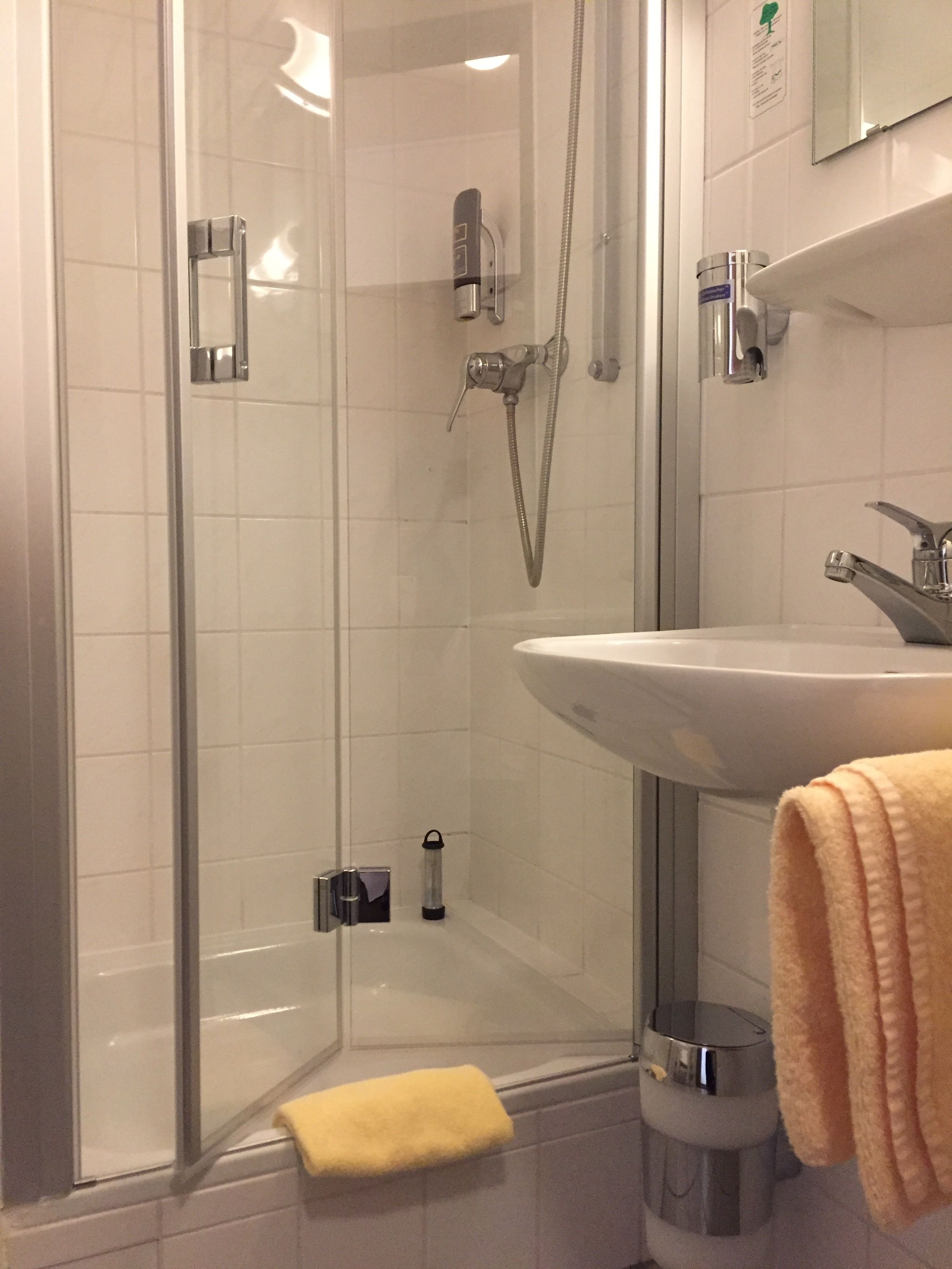 Un baño con ducha acristalada, lavabo blanco y una toalla amarilla en el suelo.