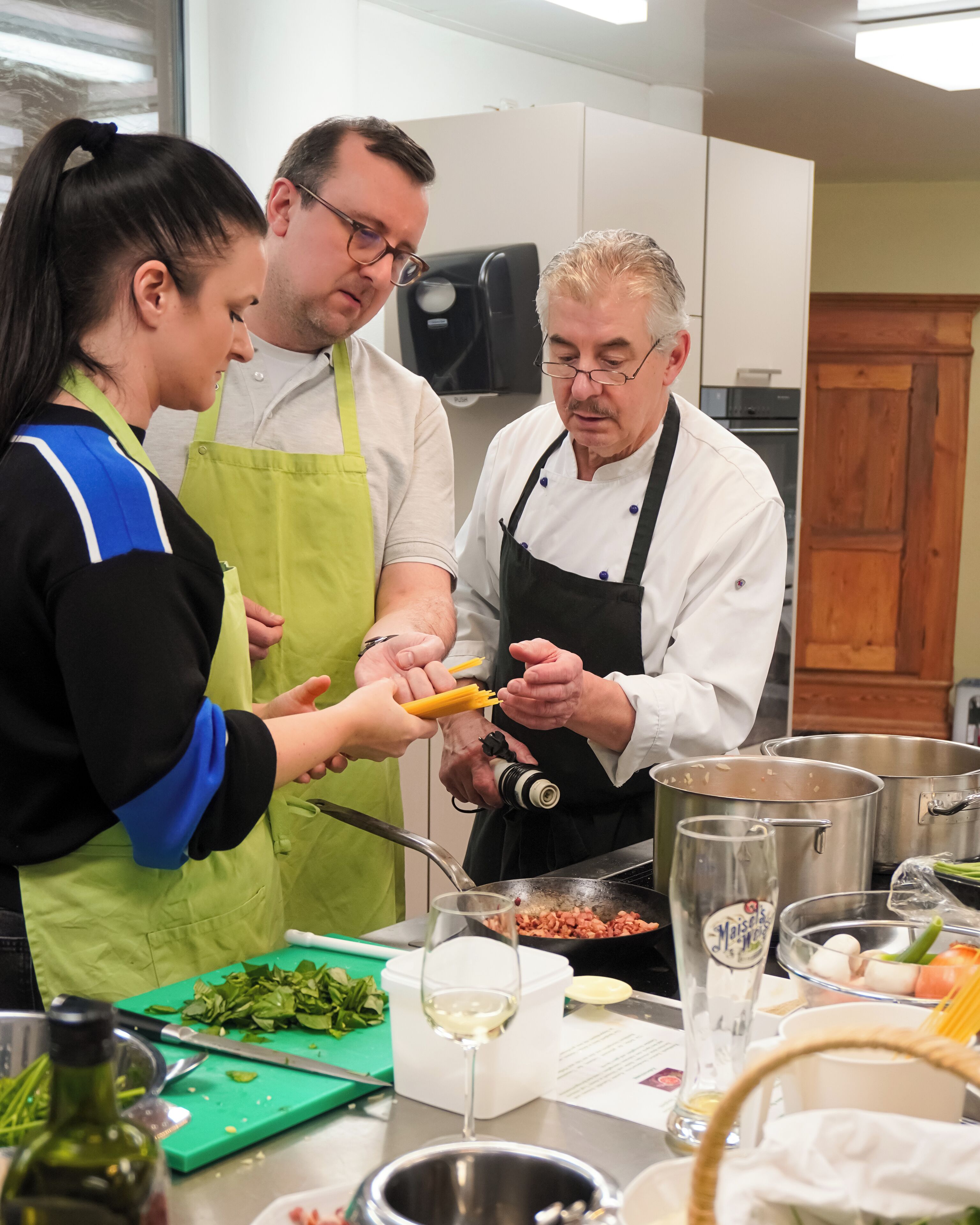 Een keuken met drie personen, waarvan er één een koksschort draagt, bereidt eten.