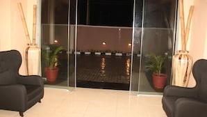 A modern lobby with two black armchairs, a glass partition, and potted plants. - TOC Hotel (Lekki)