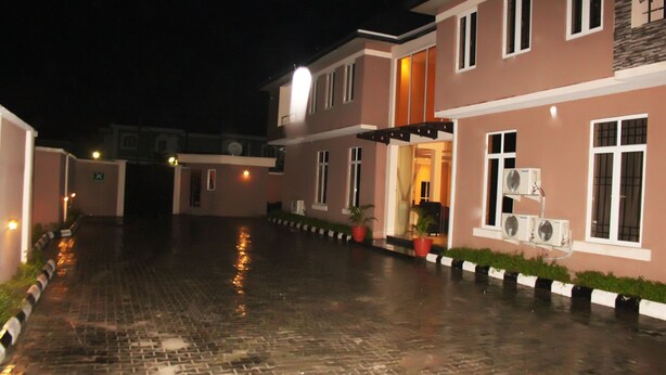 A building with multiple floors, a paved entrance area, and potted plants along the pathway. - TOC Hotel (Lekki)