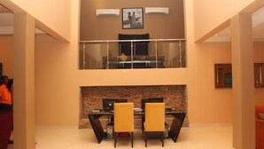 A dining area with a glass table and chairs, a fireplace, and a high ceiling with a balcony. - TOC Hotel (Lekki)
