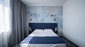 Une chambre à coucher avec un lit, des rideaux, un mur orné d’un motif d’arbre, deux lampes de chevet et une table de chevet avec une bouteille.