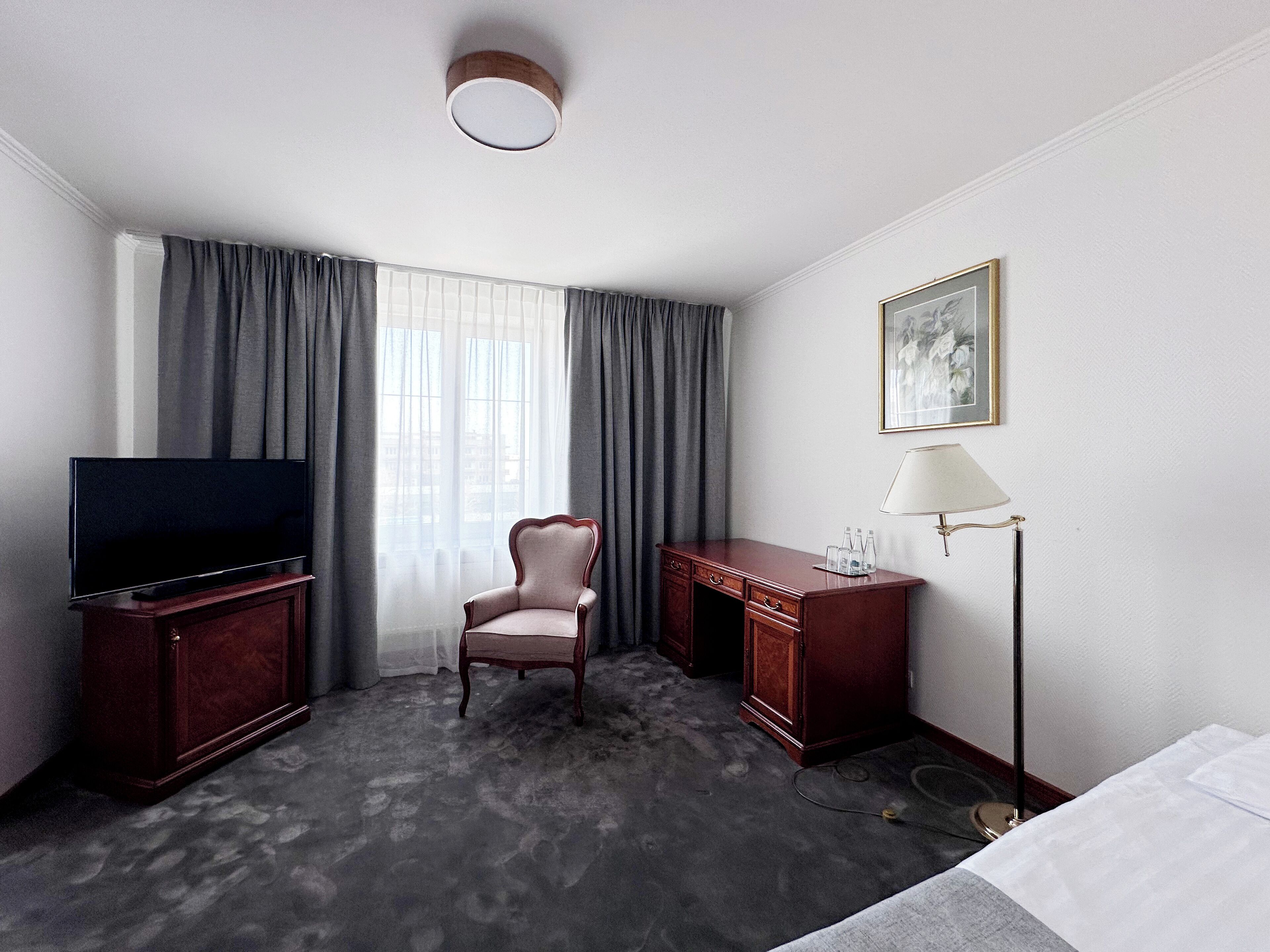 Habitación de hotel con televisión de pantalla plana, escritorio, silla, lámpara y cama.