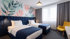 A hotel room with two beds, a desk, a chair, a large window with curtains, and a wall with a leafy pattern. - Hotel Szydlowski (Gdansk)