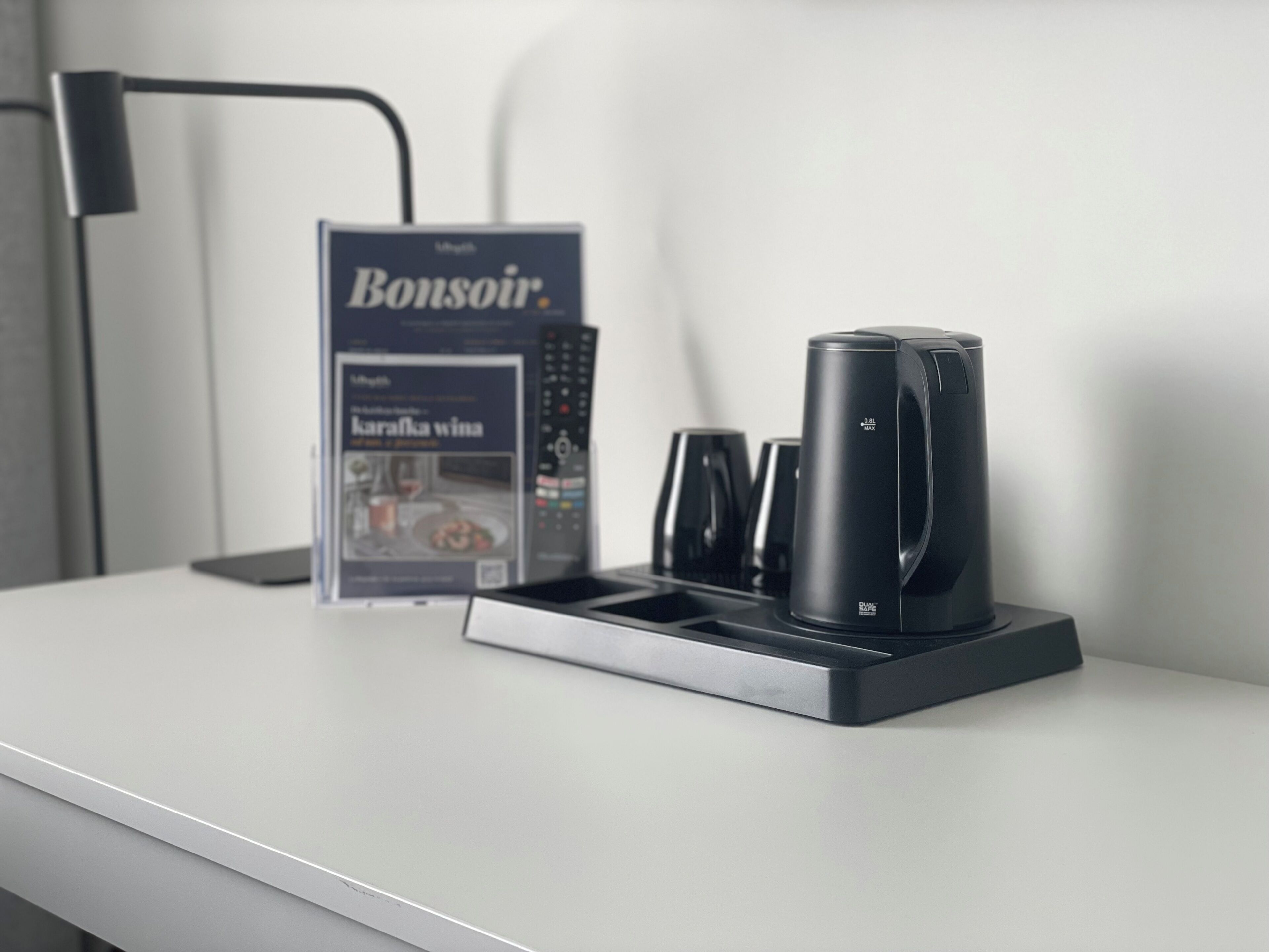 A coffee machine, a remote control, and a magazine on a white table.