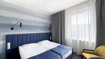 A hotel room with a bed, a chair, a window with curtains, and a wall with a textured design.