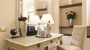 A hotel room with a white desk, a chair, a mirror, a lamp, a vase with flowers, a globe, and a trash can.