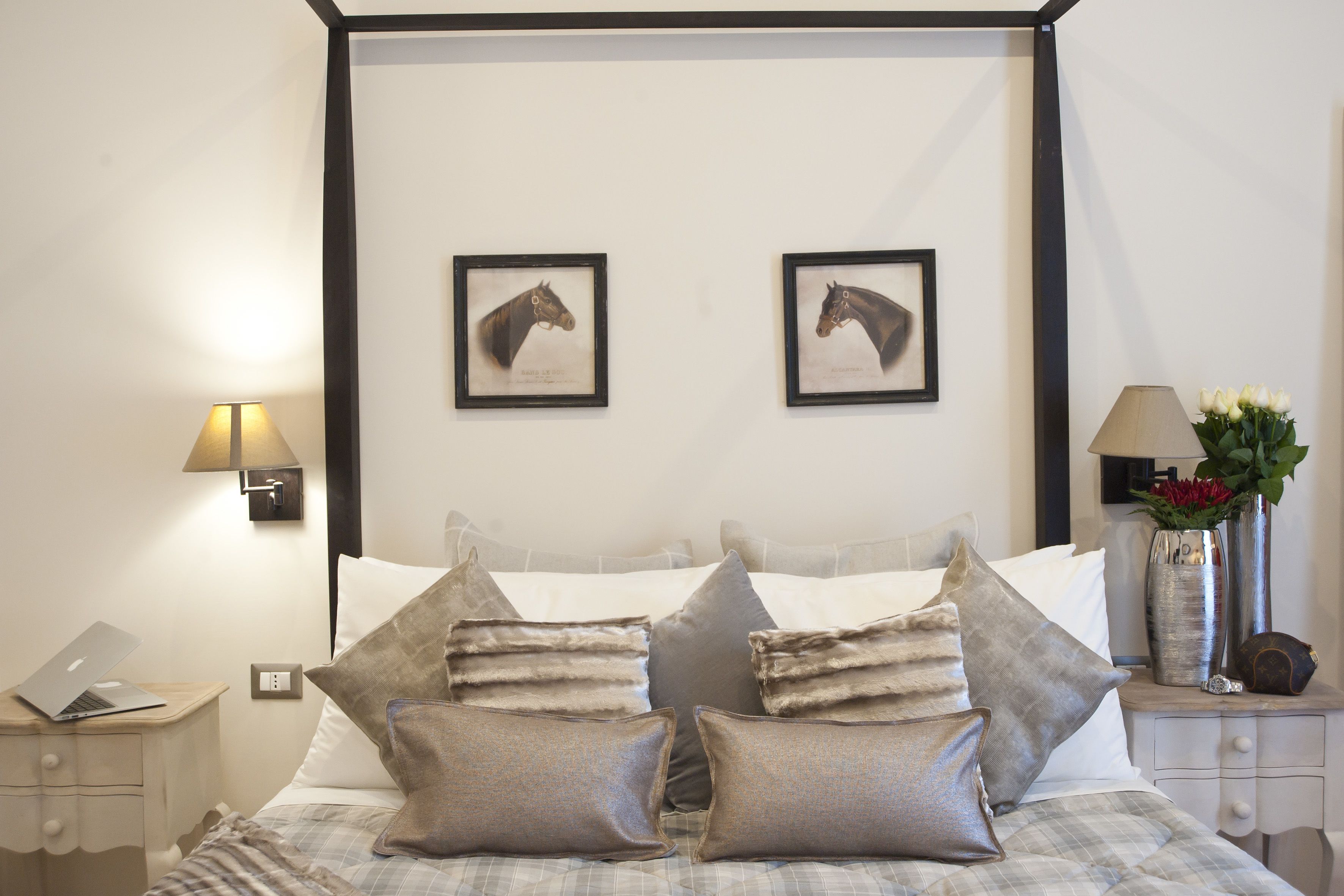 A neatly made bed with pillows, a bedside table with a lamp, and two framed horse head pictures on the wall.