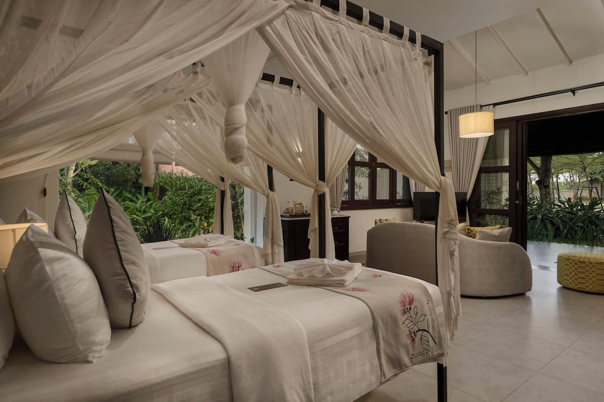 A bedroom with a canopy bed, a sofa, and a view of greenery outside.