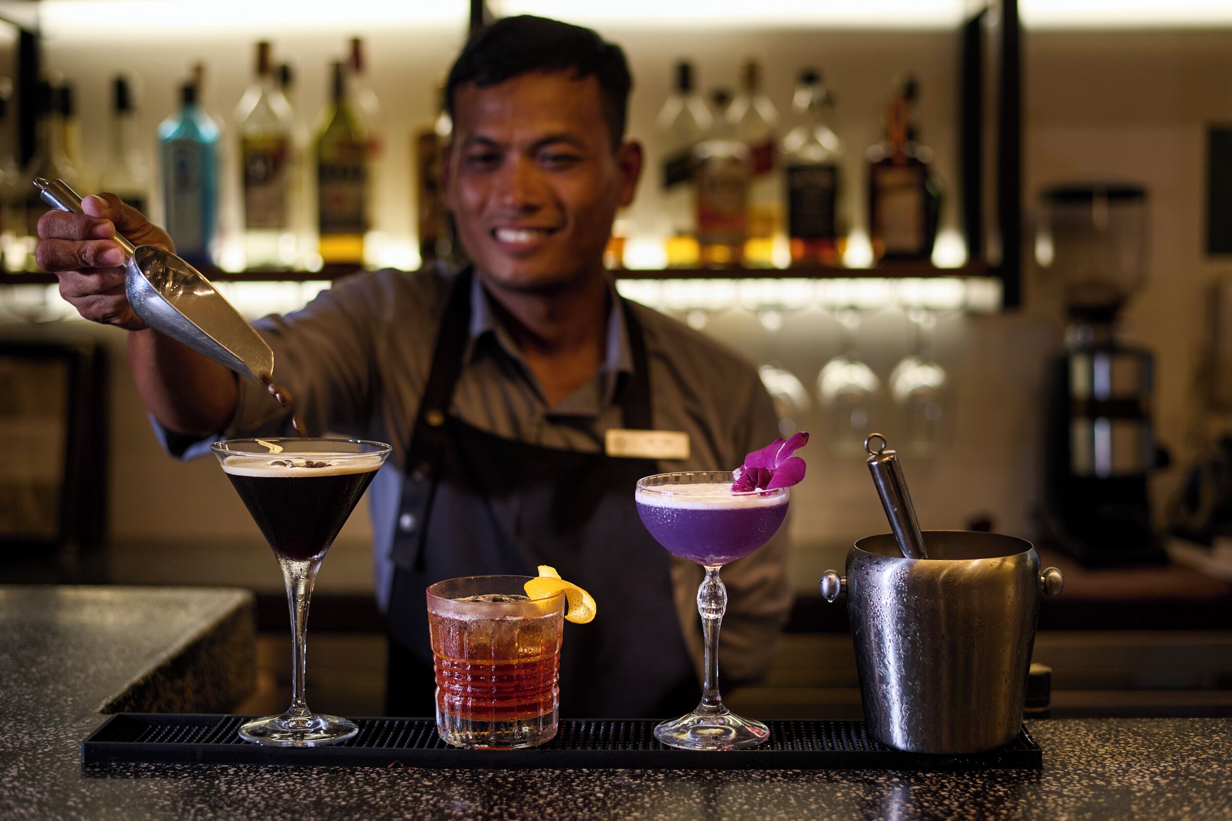 A bartender preparing drinks at a bar with a variety of bottles in the background.