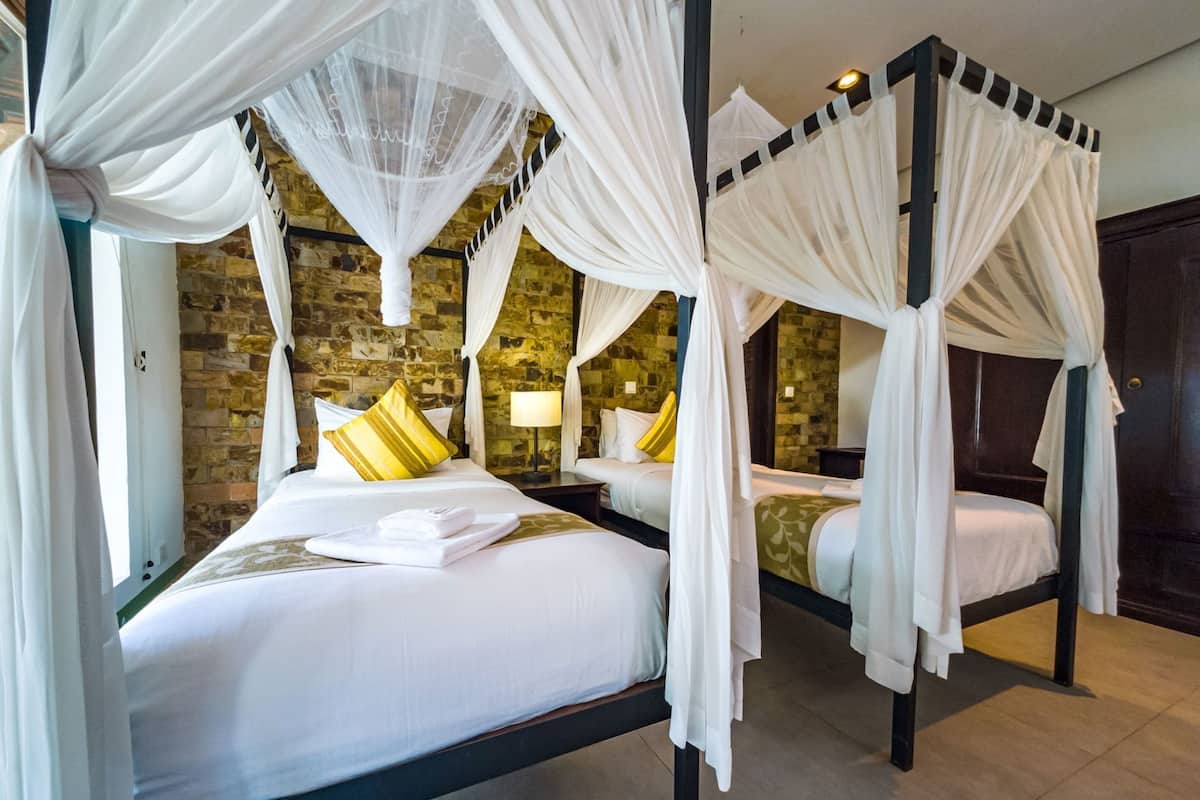 A four-poster bed with white linens and yellow pillows, a stone wall, and a wooden door.