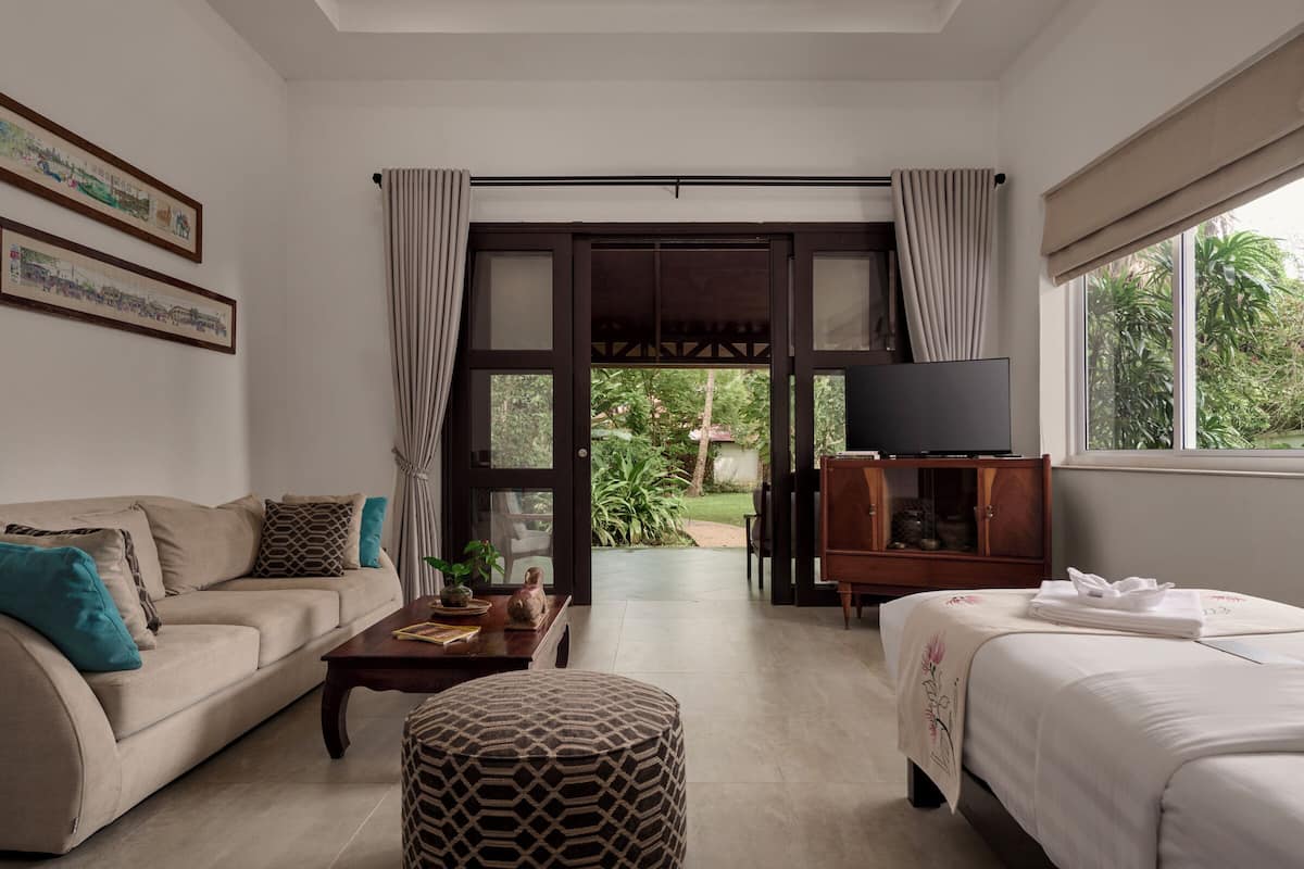 A modern hotel room with a sofa, a bed, a TV, and a view of the garden.