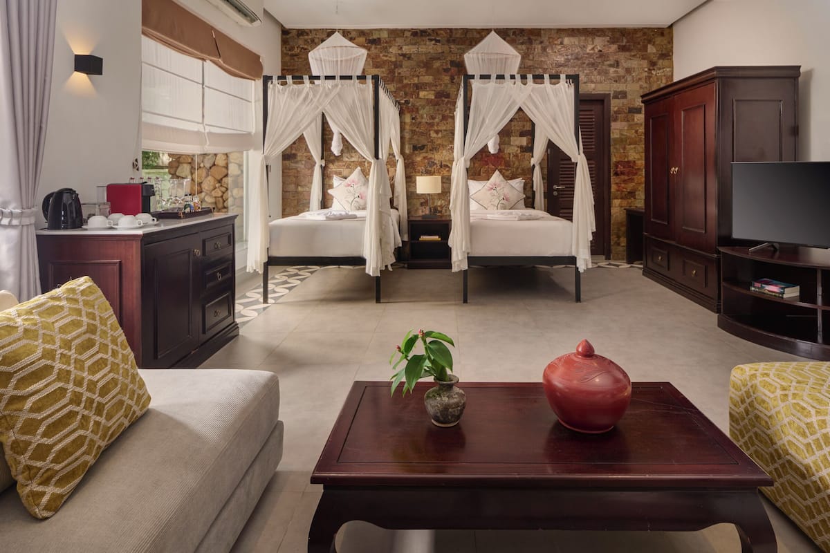 A hotel room with two beds, a TV, a coffee machine, and a small table with a vase and a pot.