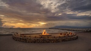 A circular stone fire pit with seating around it on a beach, overlooking the sea and a pier. - Samanea Beach Resort & Spa (Kep)