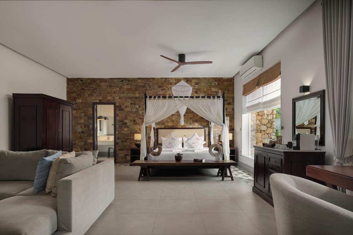 A bedroom with a canopy bed, a ceiling fan, and a stone wall.